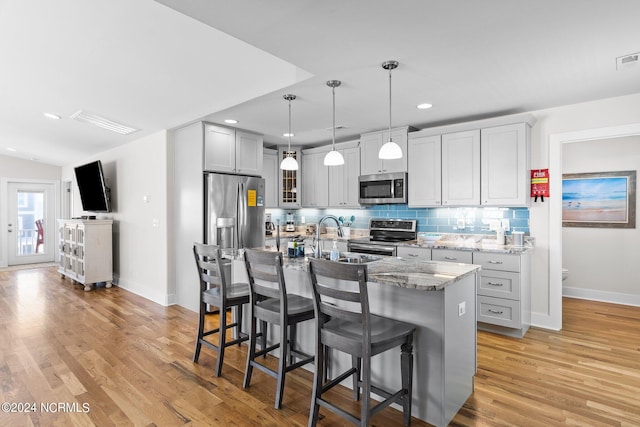 kitchen featuring an island with sink, stone countertops, decorative light fixtures, appliances with stainless steel finishes, and light hardwood / wood-style floors