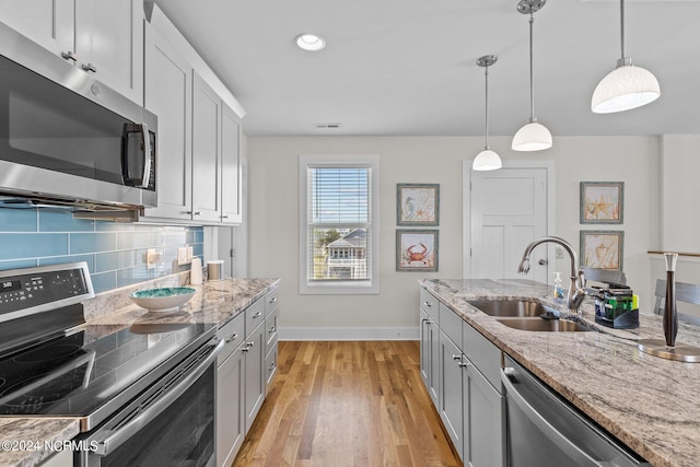 kitchen featuring appliances with stainless steel finishes, light stone countertops, light wood-type flooring, decorative light fixtures, and sink