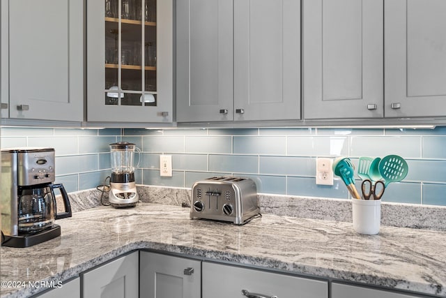 room details with backsplash, light stone countertops, and gray cabinets