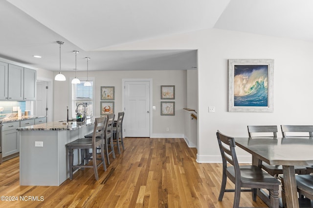 kitchen featuring pendant lighting, light hardwood / wood-style floors, sink, an island with sink, and stone counters