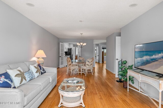 living room featuring an inviting chandelier, light hardwood / wood-style floors, and a textured ceiling