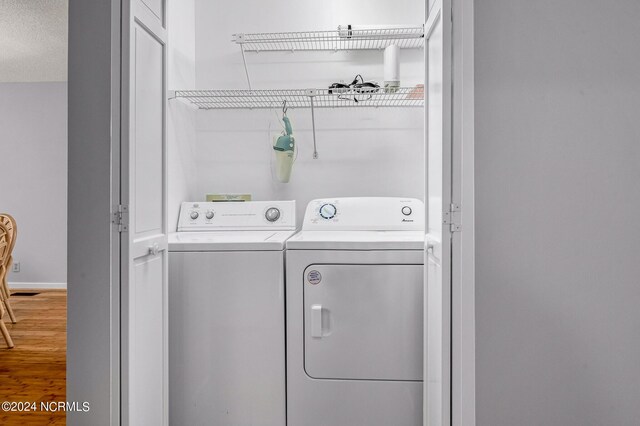 laundry area with washing machine and clothes dryer, wood-type flooring, and a textured ceiling