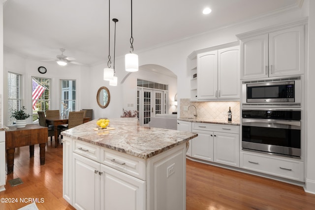 kitchen featuring white cabinetry, a center island, hanging light fixtures, stainless steel appliances, and light wood-type flooring