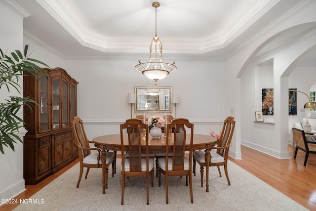 dining area with light hardwood / wood-style floors, crown molding, and a tray ceiling