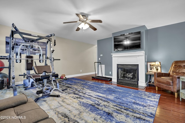 workout room featuring a fireplace with flush hearth, wood finished floors, ceiling fan, and baseboards