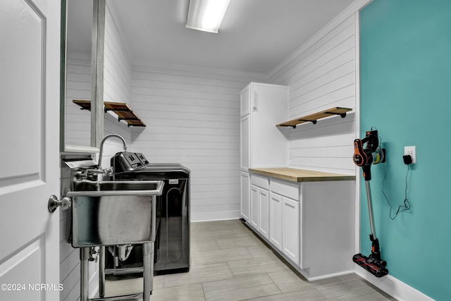 clothes washing area with cabinets, wooden walls, ornamental molding, and washing machine and clothes dryer