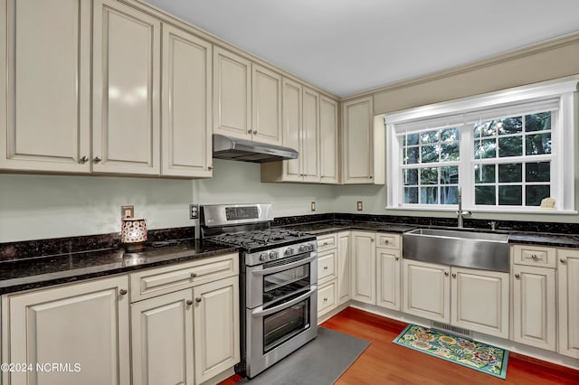 kitchen with dark stone counters, light wood-type flooring, sink, double oven range, and cream cabinets