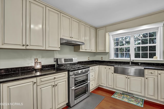 kitchen with cream cabinetry, under cabinet range hood, wood finished floors, a sink, and range with two ovens