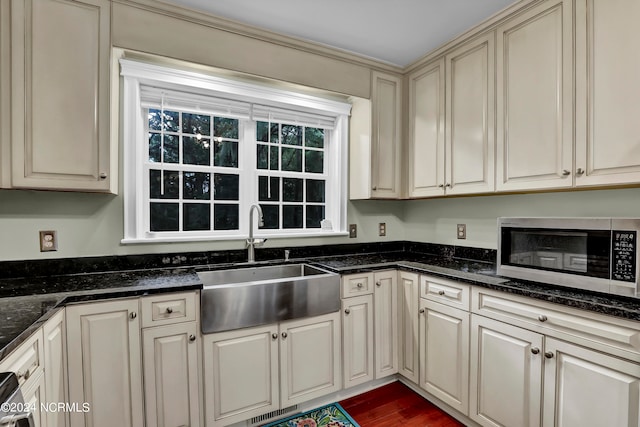 kitchen with dark hardwood / wood-style flooring, dark stone countertops, cream cabinets, and sink