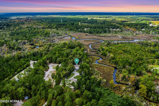 aerial view at dusk featuring a wooded view and a water view