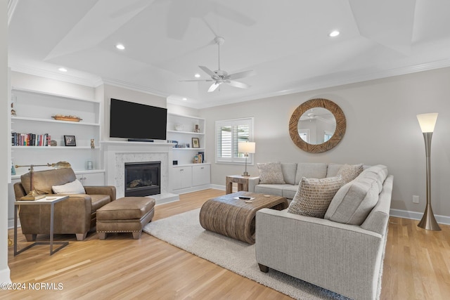 living room featuring a premium fireplace, light wood-type flooring, ceiling fan, and ornamental molding