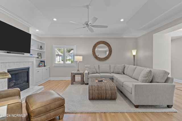 living room featuring ceiling fan, light hardwood / wood-style flooring, crown molding, and a high end fireplace