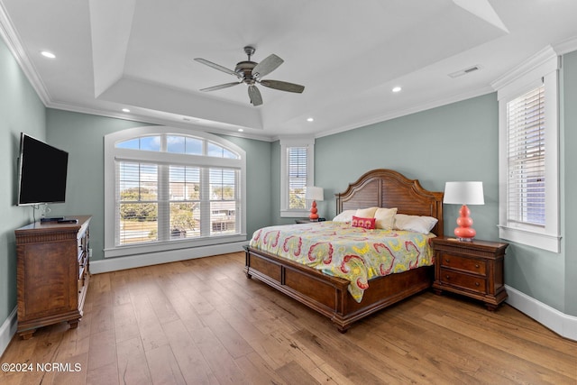 bedroom featuring light wood-type flooring, crown molding, ceiling fan, and a raised ceiling