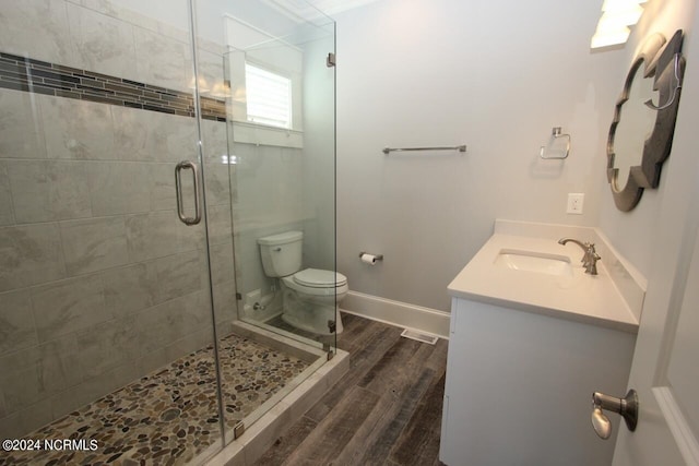 bathroom with wood-type flooring, a shower with shower door, vanity, and toilet