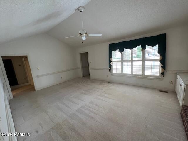 unfurnished bedroom with light carpet, vaulted ceiling, ceiling fan, and a textured ceiling