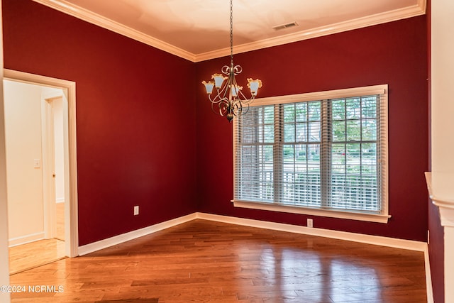 empty room with hardwood / wood-style floors, an inviting chandelier, and ornamental molding