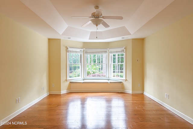 spare room featuring a raised ceiling, ceiling fan, and light hardwood / wood-style floors