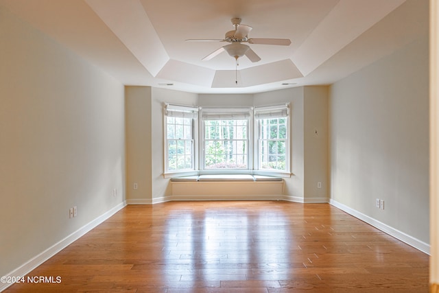 empty room with a raised ceiling, ceiling fan, and light hardwood / wood-style floors