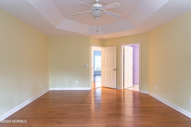 unfurnished room featuring a tray ceiling, ceiling fan, and hardwood / wood-style flooring