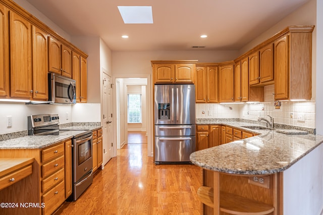 kitchen featuring a skylight, light stone countertops, sink, stainless steel appliances, and light wood-type flooring