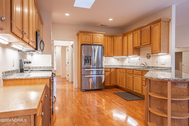 kitchen with a skylight, sink, appliances with stainless steel finishes, and light hardwood / wood-style flooring