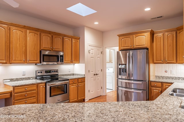 kitchen with backsplash, a skylight, light stone counters, stainless steel appliances, and washer / clothes dryer