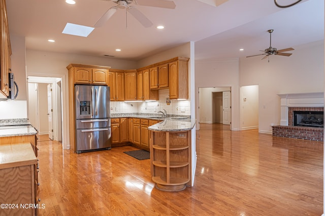 kitchen featuring a skylight, light hardwood / wood-style flooring, ceiling fan, appliances with stainless steel finishes, and light stone counters