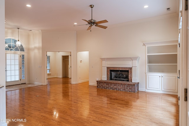 unfurnished living room with a fireplace, ceiling fan with notable chandelier, light hardwood / wood-style floors, and crown molding