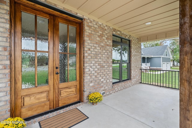 doorway to property featuring covered porch, french doors, and brick siding