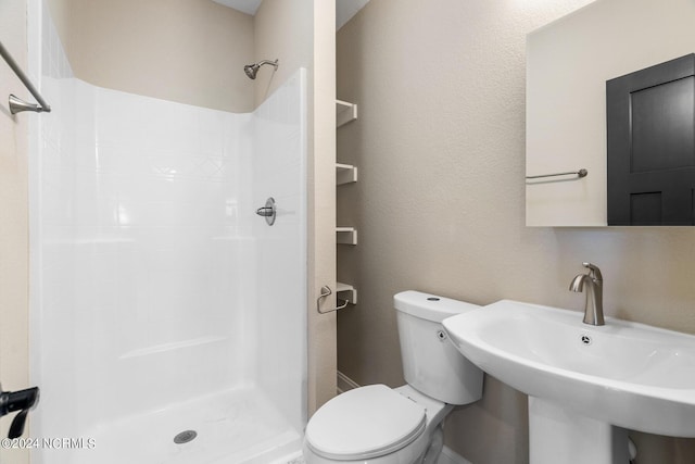 bathroom with toilet, a shower stall, a sink, and a textured wall