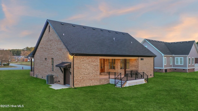 back of house at dusk featuring crawl space, brick siding, a yard, and roof with shingles