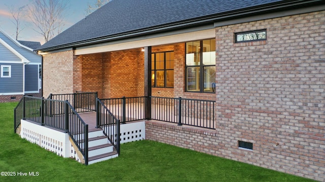 rear view of house with a shingled roof, crawl space, brick siding, and a lawn