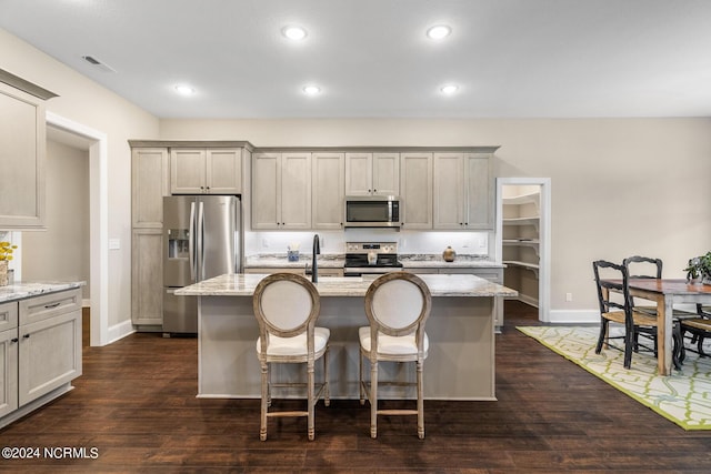 kitchen featuring an island with sink, light stone counters, stainless steel appliances, and dark wood finished floors