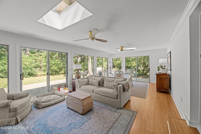 living room featuring ceiling fan, a skylight, crown molding, and light hardwood / wood-style floors