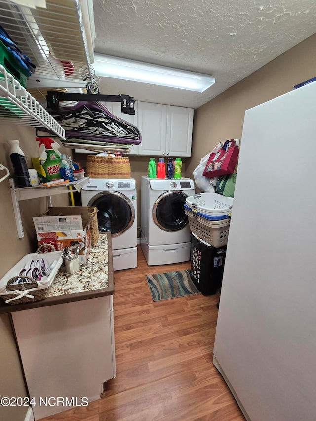 laundry room with light hardwood / wood-style flooring, a textured ceiling, cabinets, and separate washer and dryer