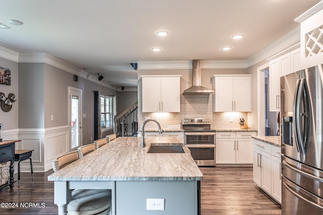 kitchen featuring white cabinets, a kitchen island with sink, wall chimney range hood, stainless steel appliances, and dark hardwood / wood-style floors