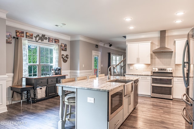 kitchen featuring white cabinets, a center island with sink, stainless steel appliances, and wall chimney exhaust hood