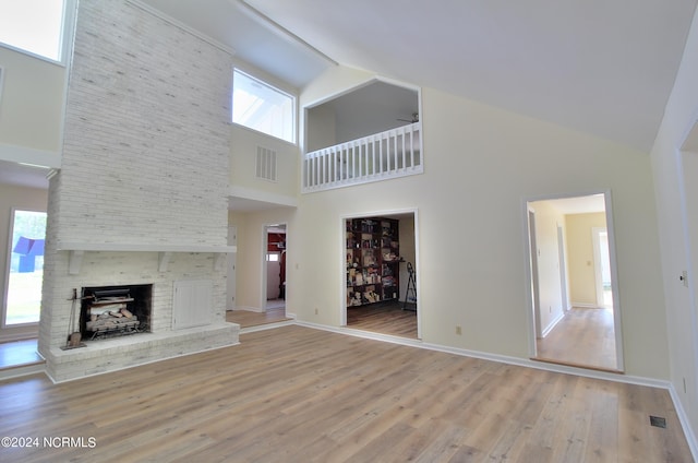 unfurnished living room with a brick fireplace, a high ceiling, and light wood-type flooring