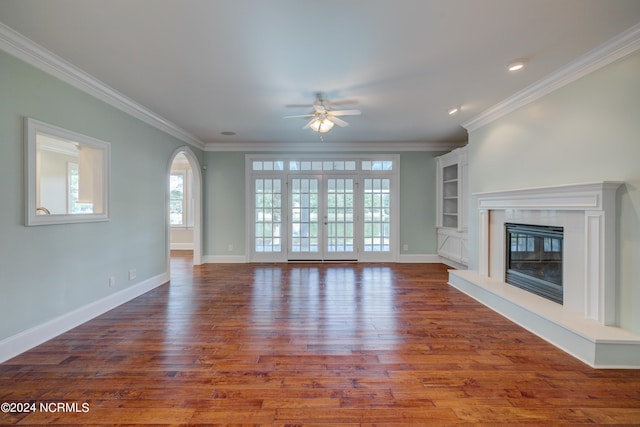 unfurnished living room featuring crown molding, built in shelves, ceiling fan, and dark wood-type flooring