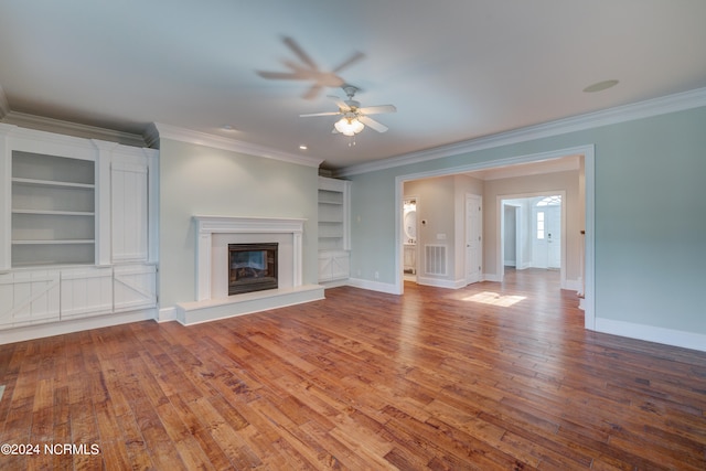 unfurnished living room with wood-type flooring, ceiling fan, built in shelves, and crown molding