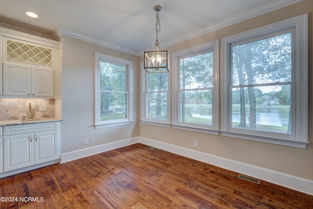 unfurnished dining area featuring a chandelier, plenty of natural light, dark wood-type flooring, and crown molding