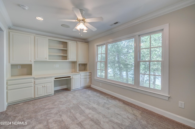 unfurnished office with ornamental molding, built in desk, ceiling fan, and light colored carpet