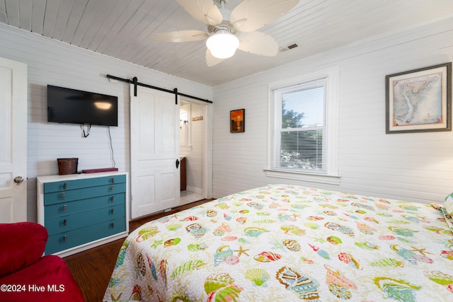 bedroom with a barn door, ceiling fan, and dark hardwood / wood-style floors