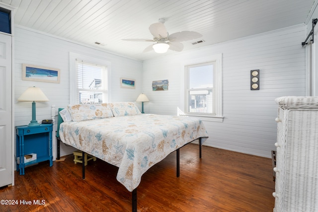 bedroom featuring a barn door, ceiling fan, crown molding, and dark hardwood / wood-style flooring