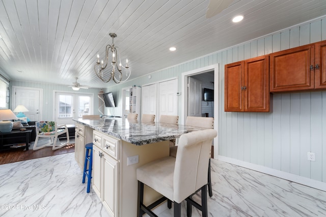 kitchen with light stone countertops, hanging light fixtures, a kitchen breakfast bar, and a kitchen island with sink