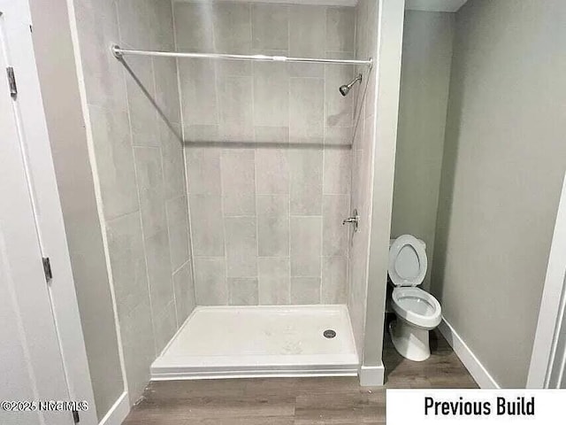 bathroom with hardwood / wood-style flooring, toilet, and tiled shower