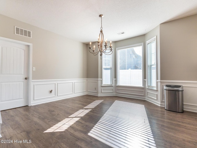 unfurnished dining area with dark hardwood / wood-style flooring, a textured ceiling, and a notable chandelier