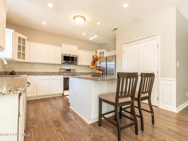 kitchen featuring hardwood / wood-style floors, a center island, stone counters, white cabinetry, and stainless steel appliances