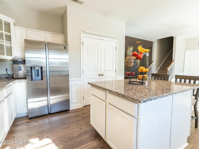 kitchen with light stone countertops, stainless steel fridge with ice dispenser, a center island, and white cabinetry