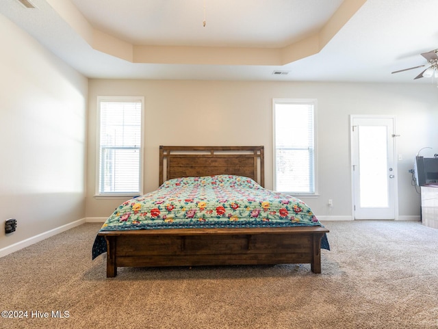 carpeted bedroom featuring ceiling fan and a raised ceiling